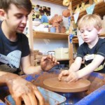 Child making a pot on the pottery wheel under the guidance of Ethan the potter