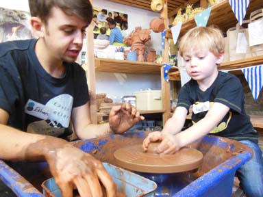 Child making a pot on the pottery wheel under the guidance of Ethan the potter